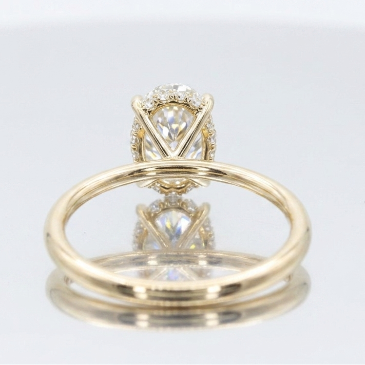 Close-up of an oval lab-grown diamond held by four prongs, featuring a hidden halo of accent diamonds visible from the side, set on a 14K yellow gold mounting